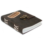 Un carnet grimoire en cuir marron foncé embossé du mot "Confession" sur une pièce de cuir clair, fermé par un loquet métallique en laiton et doté d'une reliure artisanale à lacets blancs sur fond blanc.