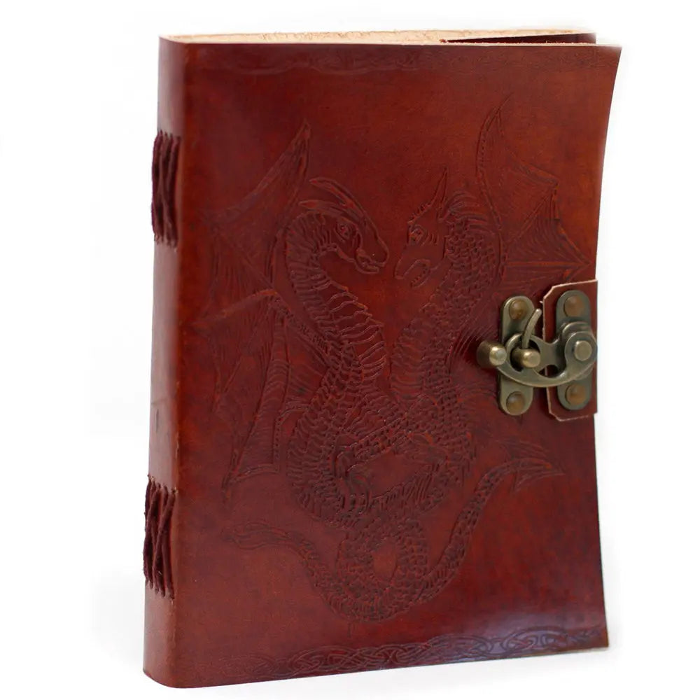 La couverture d'un carnet grimoire en cuir marron clair ornée d'un double motif de dragons ailés embossés, fermée par un loquet métallique en laiton et dotée d'une reliure artisanale à lacets assortis.