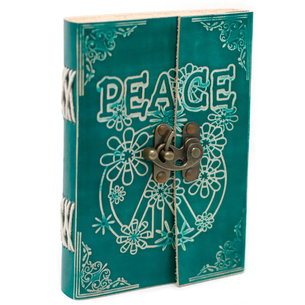 La couverture d'un carnet grimoire en cuir turquoise embossé du mot "PEACE" et d'un symbole de paix fleuri, maintenue par un loquet métallique en laiton avec une reliure artisanale à lacets blancs.