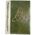 La couverture d'un carnet grimoire artisanal conçu à partir de feuilles naturelles vertes, ornée d'une triquetra en cordelette et d'une reliure végétale intégrant une branche fine, sur fond blanc.