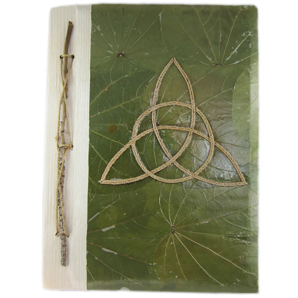 La couverture d'un carnet grimoire artisanal conçu à partir de feuilles naturelles vertes, ornée d'une triquetra en cordelette et d'une reliure végétale intégrant une branche fine, sur fond blanc.