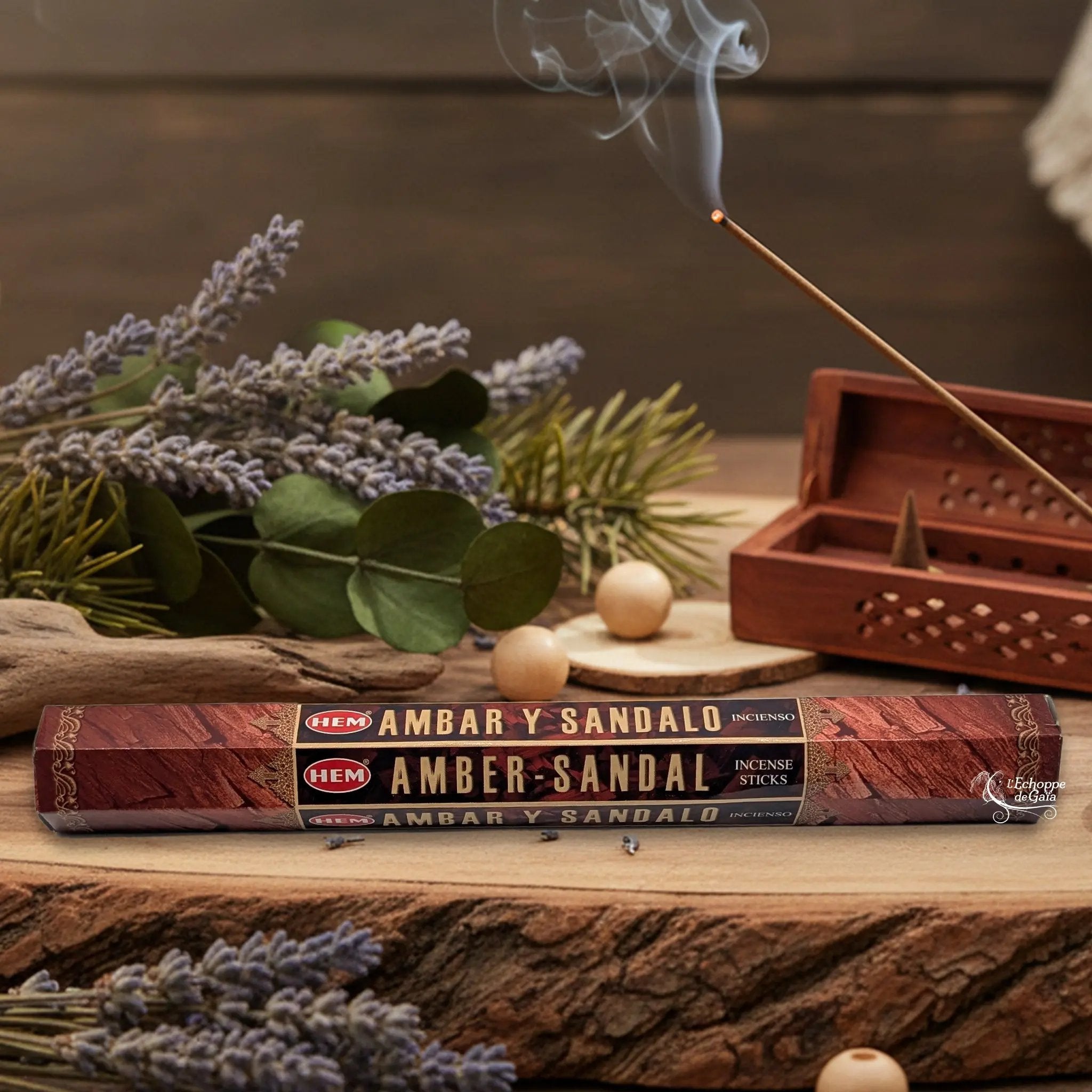 Boîte d'encens HEM "Amber-Sandal / Ambar y Sandalo" posée sur du bois avec de la lavande et un bâton d'encens fumant.