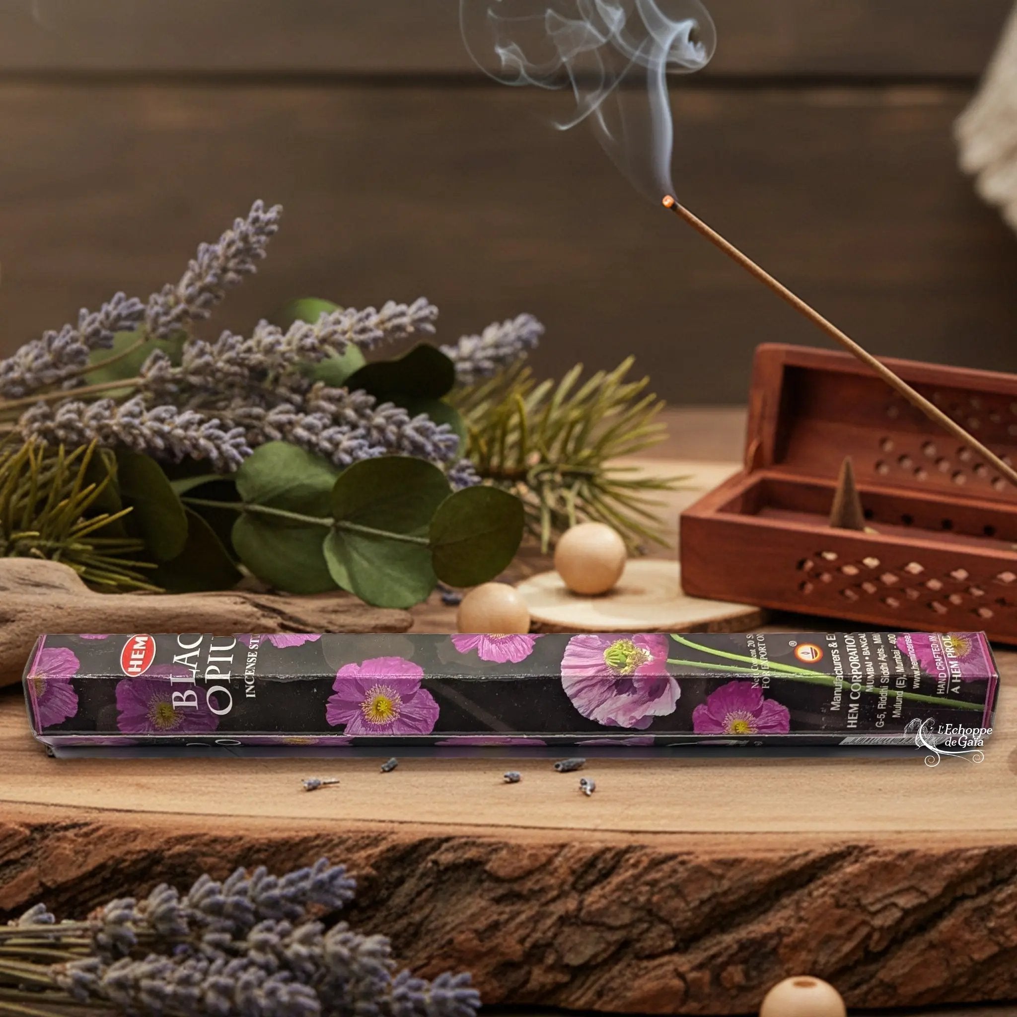 Boîte d'encens HEM "Black Opium" posée sur du bois avec de la lavande et un bâton d'encens fumant.