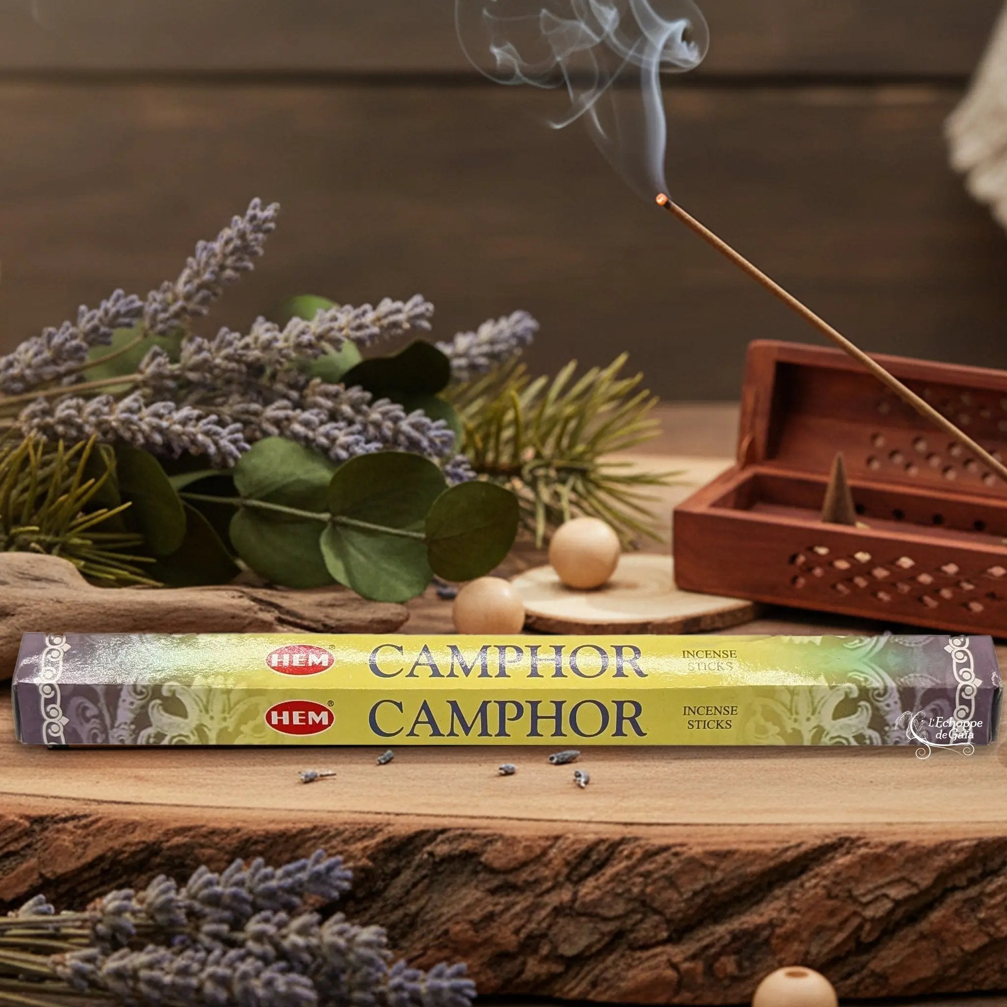 Boîte d'encens HEM "Camphor" posée sur du bois avec de la lavande et un bâton d'encens fumant.