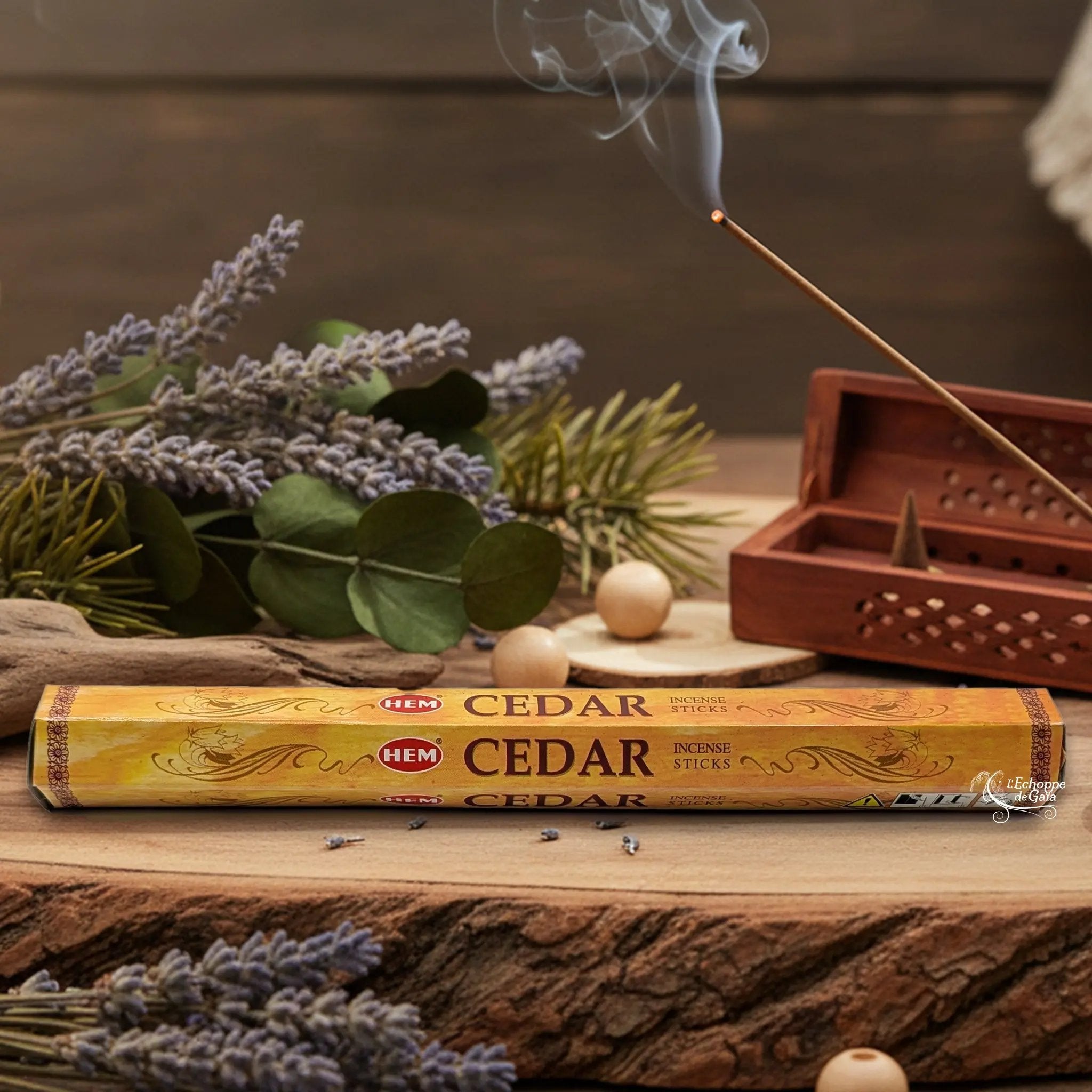 Boîte d'encens HEM "Cedar" posée sur du bois avec de la lavande et un bâton d'encens fumant.