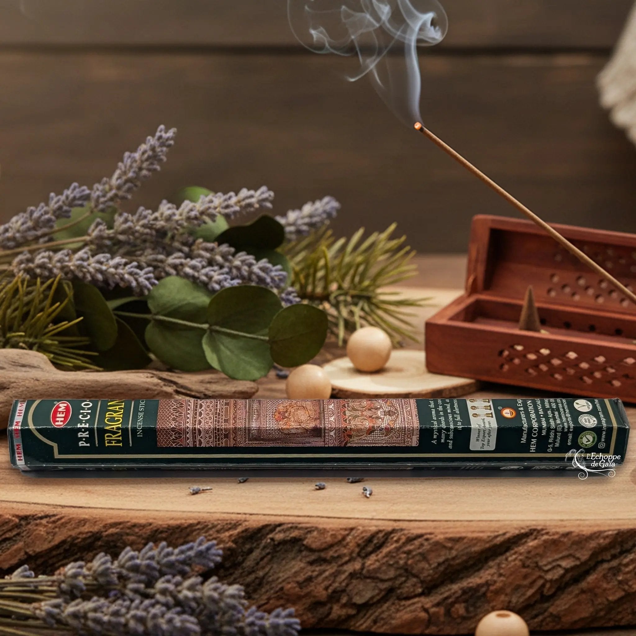 Boîte d'encens HEM "Precious Fragrance" posée sur du bois avec de la lavande et un bâton d'encens fumant.