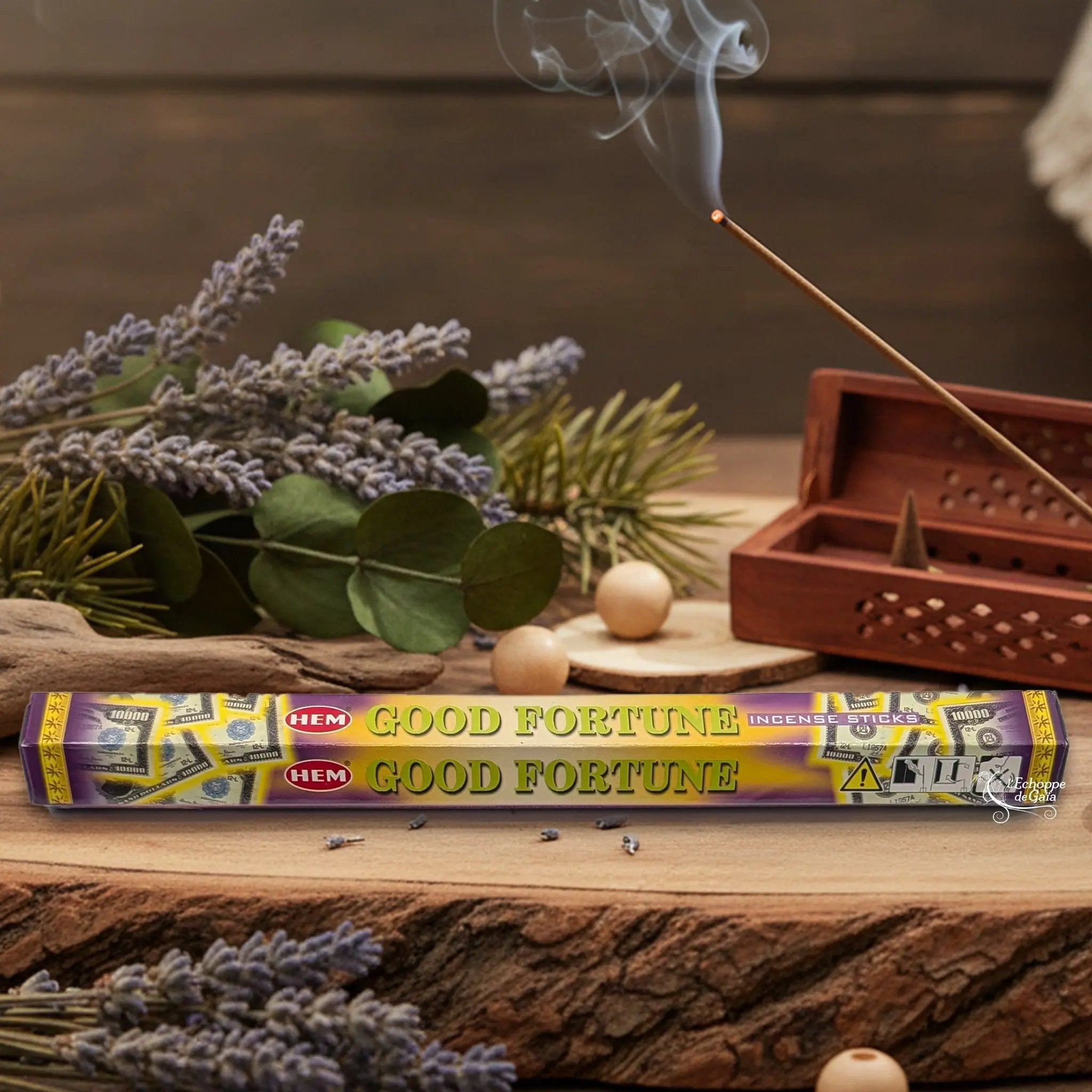 Boîte d'encens HEM "Good Fortune" posée sur du bois avec de la lavande et un bâton d'encens fumant.