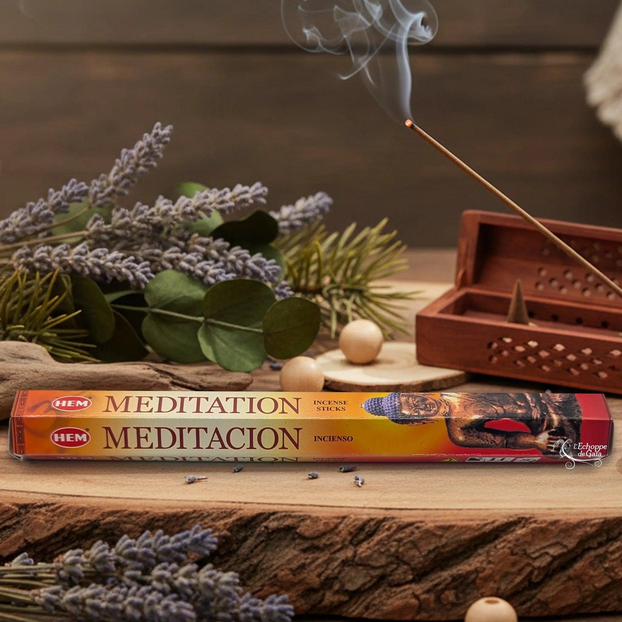 Boîte d'encens HEM "Meditation / Meditacion" posée sur du bois avec de la lavande et un bâton d'encens fumant.