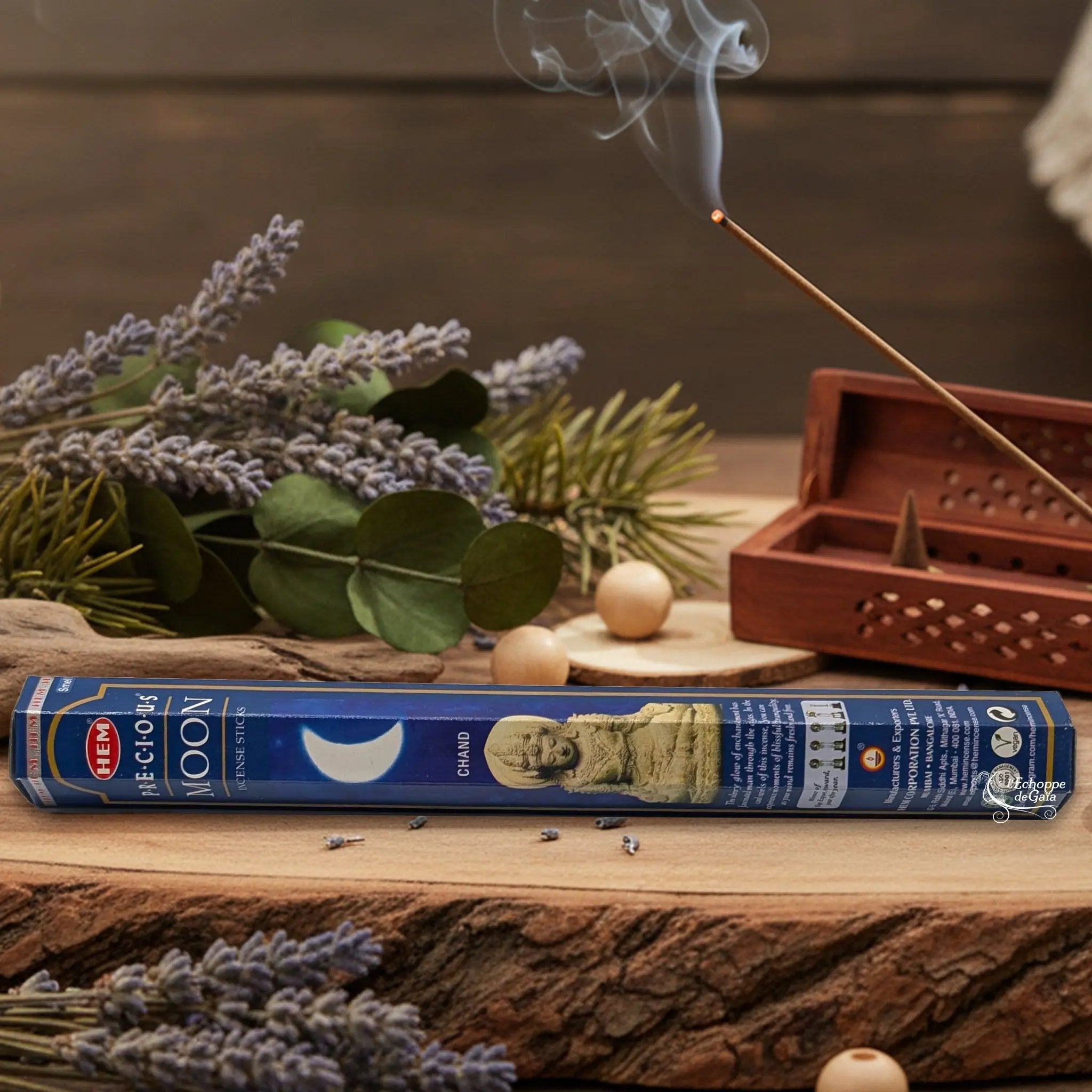 Boîte d'encens HEM "Precious Moon" posée sur du bois avec de la lavande et un bâton d'encens fumant.