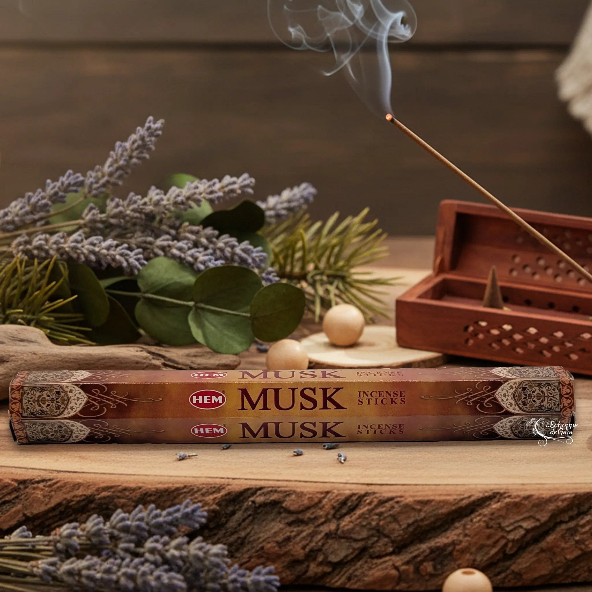 Boîte d'encens HEM "Musk" posée sur du bois avec de la lavande et un bâton d'encens fumant.