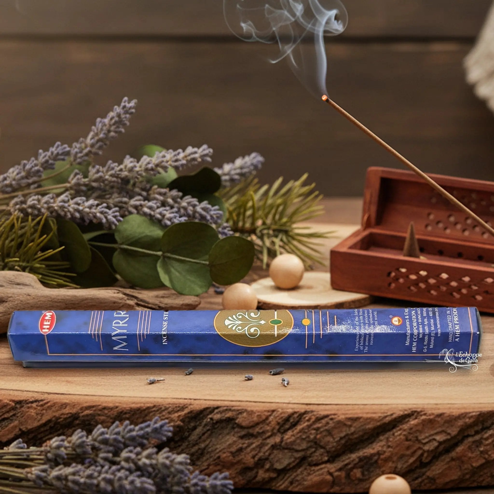 Boîte d'encens HEM "Myrrh" posée sur du bois avec de la lavande et un bâton d'encens fumant.