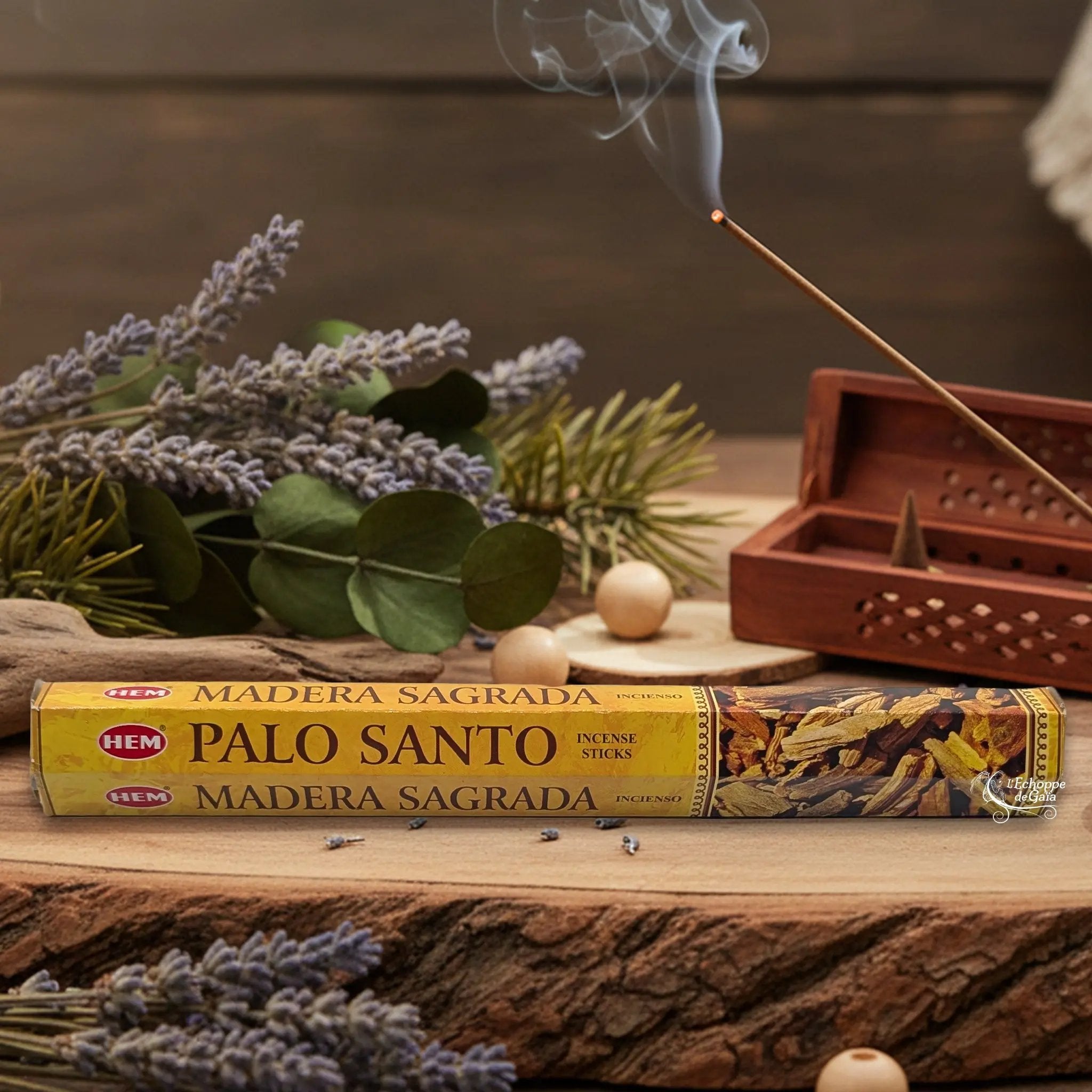 Boîte d'encens HEM "Palo Santo / Madera Sagrada" posée sur du bois avec de la lavande et un bâton d'encens fumant.