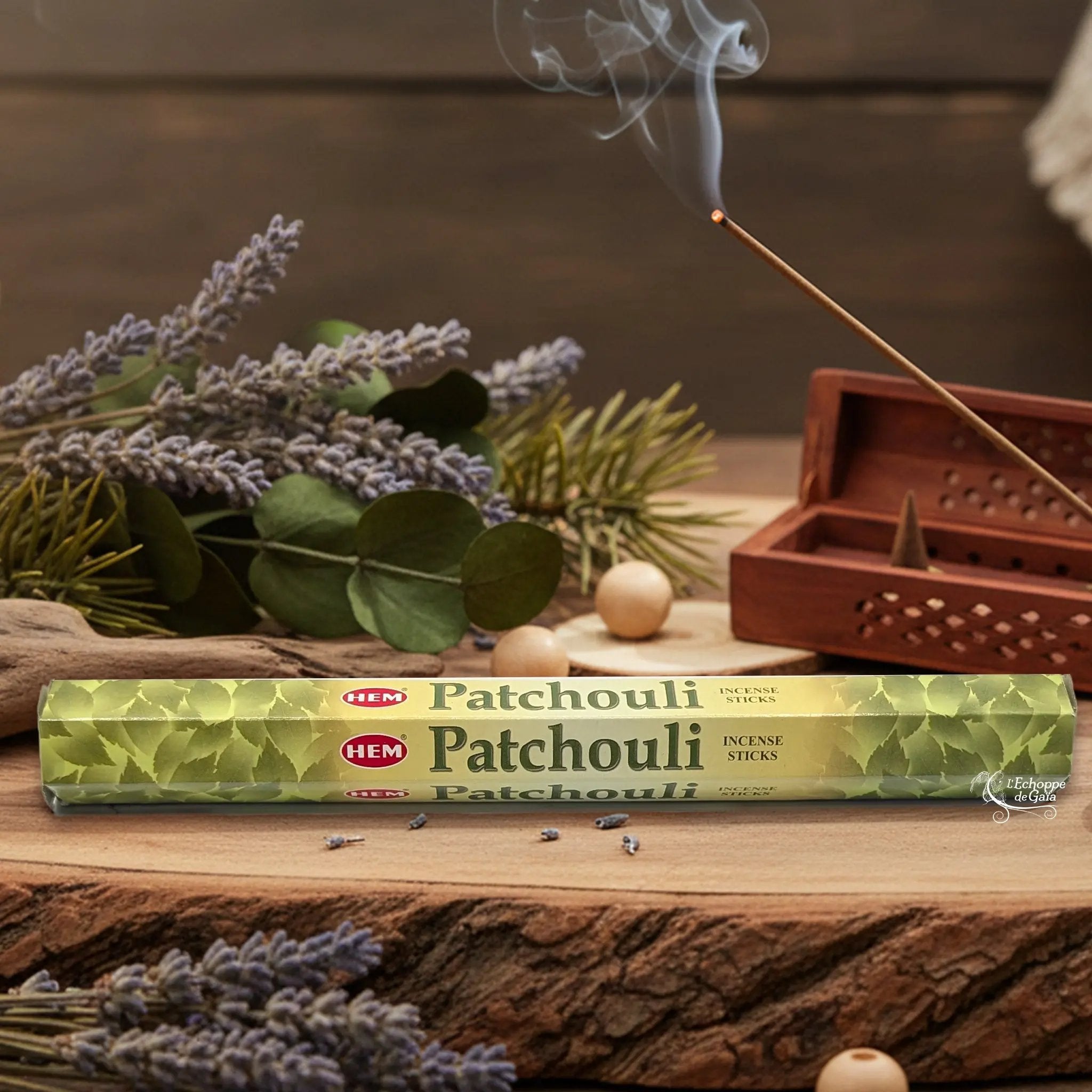Boîte d'encens HEM "Patchouli" posée sur du bois avec de la lavande et un bâton d'encens fumant.