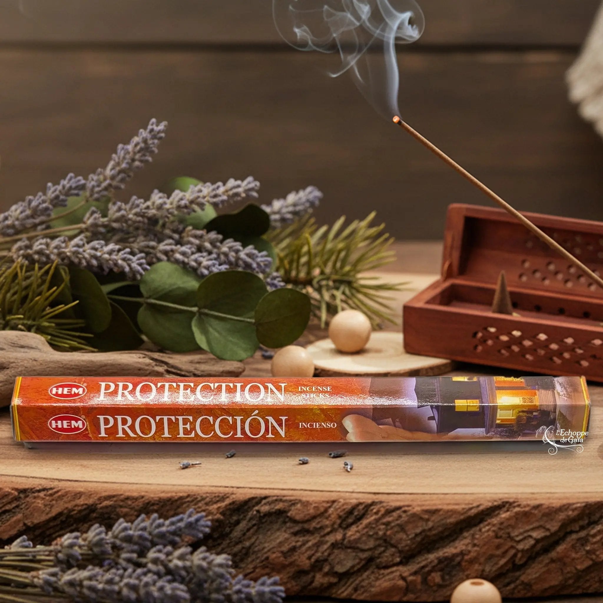 Boîte d'encens HEM "Protection / Protección" posée sur du bois avec de la lavande et un bâton d'encens fumant.
