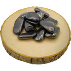 Pierres d'hématite polies, aux reflets métalliques gris foncé, disposées sur un support en bois circulaire.