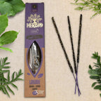 Boîte d'encens Herbio Lavande naturel violette avec trois bâtonnets à tige violette sur fond beige et feuilles vertes