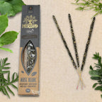 Boîte d'encens Herbio Musc Blanc naturel noire avec trois bâtonnets à tige rose sur fond beige et feuilles vertes