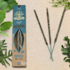 Boîte d'encens Herbio Patchouli naturel bleu avec trois bâtonnets végétaux sur fond beige et feuilles vertes