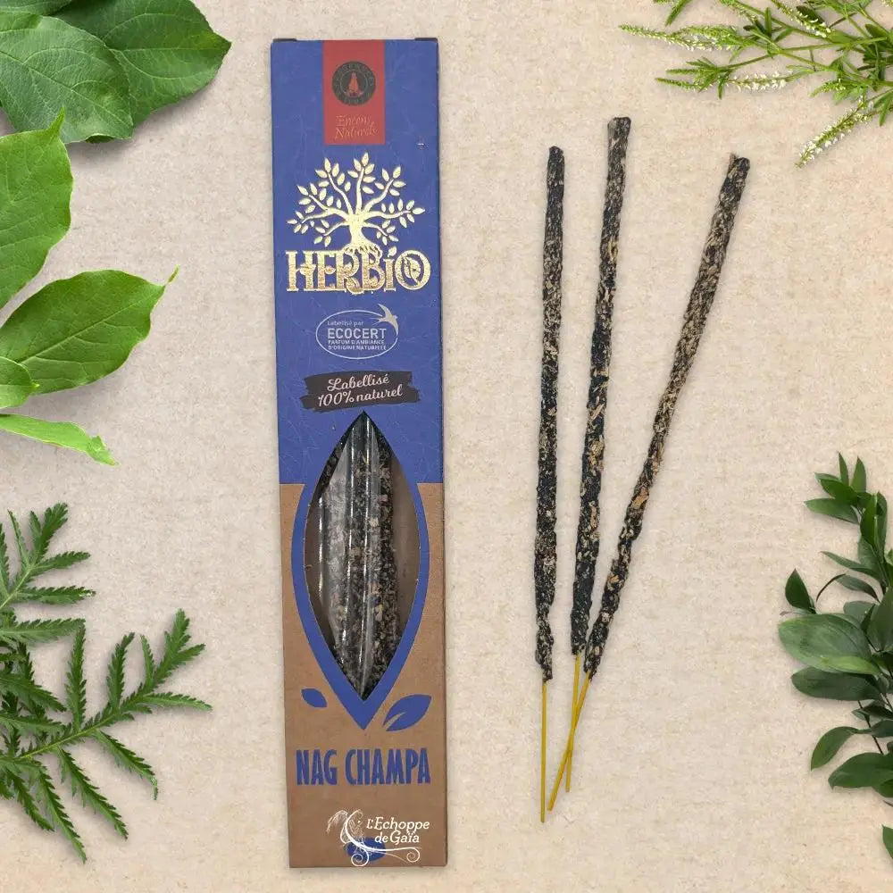 Boîte d'encens Herbio Nag Champa naturel bleu avec trois bâtonnets à tige jaune sur fond beige et feuilles vertes