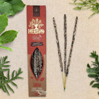 Boîte d'encens Herbio Santal naturel marron avec trois bâtonnets à tige jaune sur fond beige et feuilles vertes