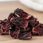 Gros plan sur des fleurs d’hibiscus séchées, aux pétales ondulés rouge foncé sur fond en bois.