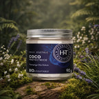 Pot en verre d'Huile Végétale Coco Protectrice Herbes et Traditions déposé sur un lit de mousse forestière avec des petites fleurs blanches et violettes.