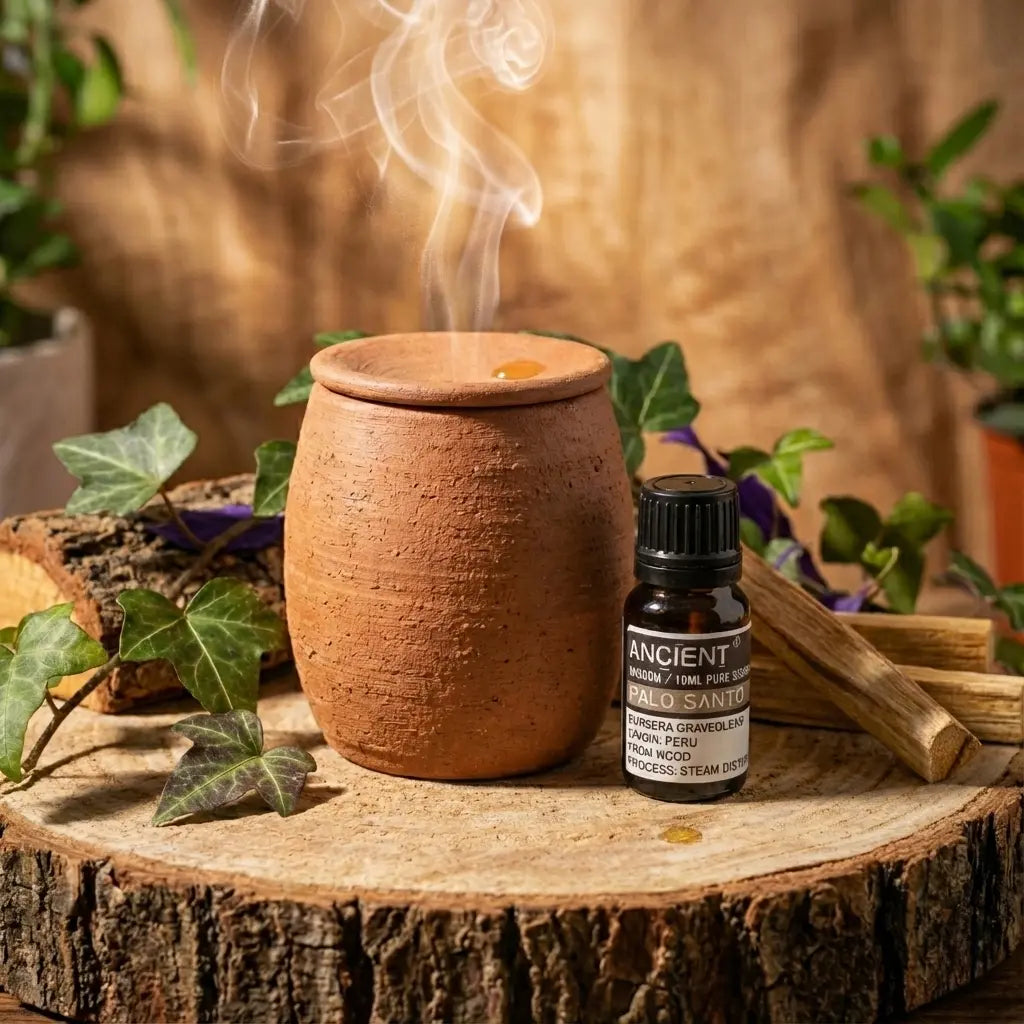Huile essentielle de palo santo 10 ml, flacon ambré à bouchon noir près d’un diffuseur en terre cuite fumant sur rondin de bois.