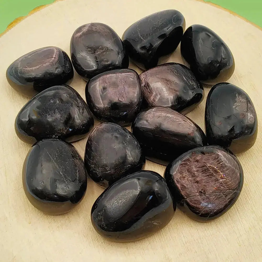 Plusieurs pierres d'hypersthène polies, affichant une couleur noire profonde avec des reflets métalliques et nacrés caractéristiques, disposées sur un socle en bois clair.