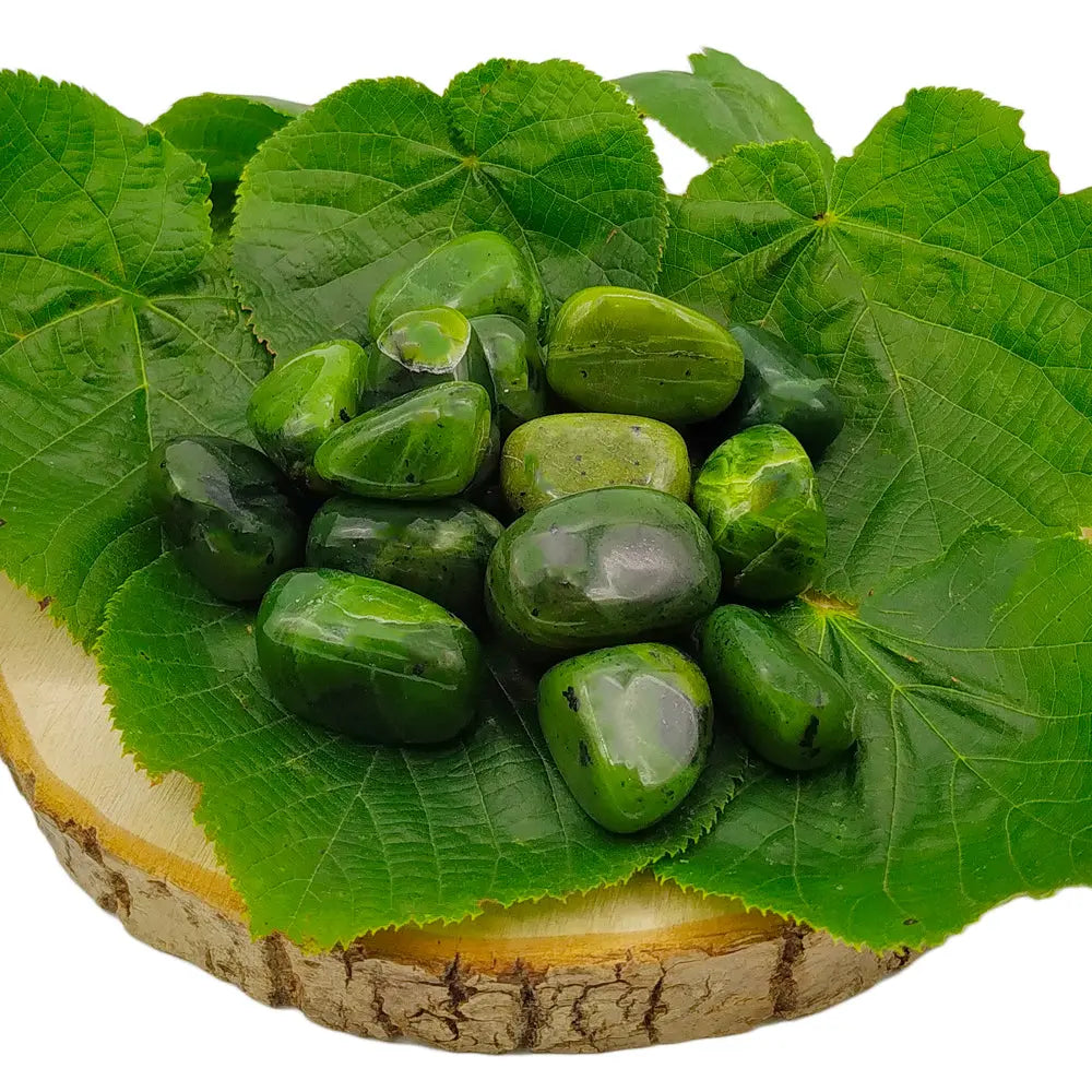 Petit tas de pierres de jade roulées aux diverses nuances de vert, disposé sur de larges feuilles vertes posées sur une rondelle de bois naturel.