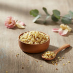 Grains d'encens de résine Jasmin, de couleur jaune-doré et beige clair, dans un petit bol en bois clair avec une cuillère, sur une planche de bois rustique.