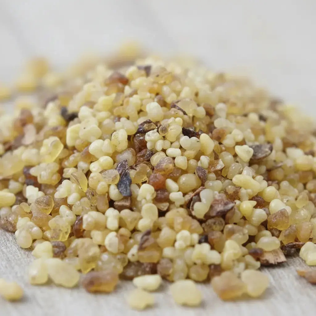 Gros plan sur un monticule de grains d'encens de résine Jasmin, montrant des billes translucides de couleur jaune clair, ambrée et brun foncé, sur une surface claire.