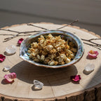 Fleurs de jasmin séchées dans une coquille d’ormeau nacrée, posées sur une tranche de bois avec cristaux et pétales de rose.