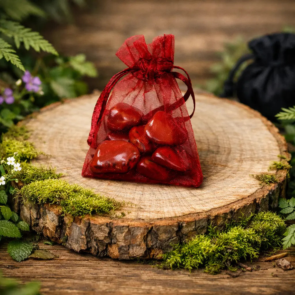 Pochette en organza rouge contenant plusieurs petites pierres de Jaspe Rouge polies de taille XS, posée sur une tranche de bois entourée de mousse.