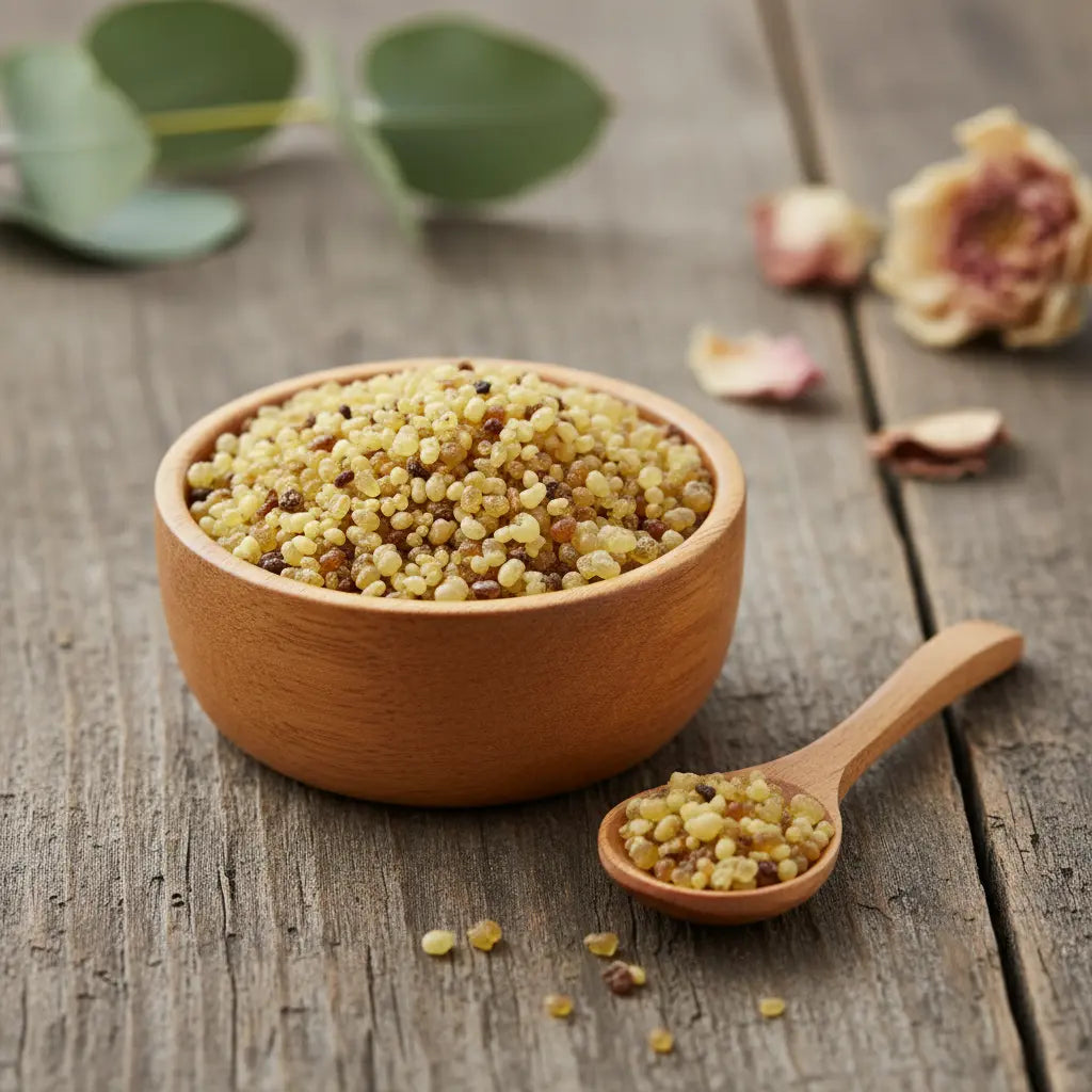 Grains d'encens de résine Jérusalem, de couleur jaune-ambre et beige, dans un petit bol en bois clair avec une cuillère, sur une planche de bois rustique.