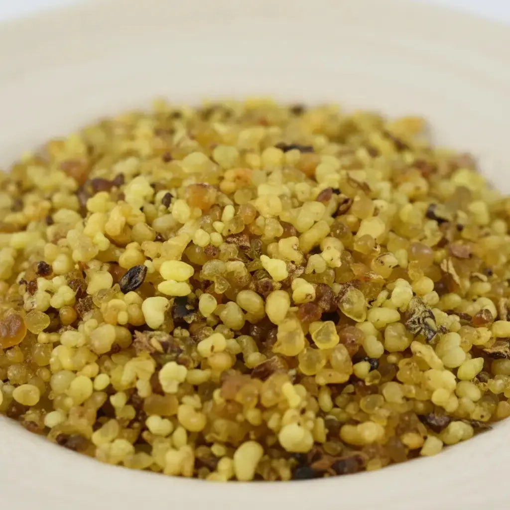 Gros plan sur un monticule de grains d'encens de résine Jérusalem, montrant des billes translucides de couleur jaune-vert doré et ambré, avec quelques grains plus foncés.