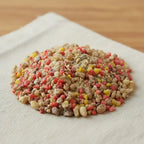 Gros plan sur un monticule de grains d'encens de résine Jésus, montrant un mélange dominant de beige, rouge corail et jaune, saupoudré de poudre de résine.