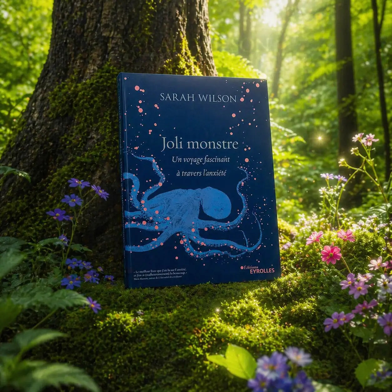 Livre bleu Joli Monstre de Sarah Wilson posé dans un sous-bois fleuri, illustré d'une pieuvre aux reflets bleutés et de points rose pâle.