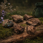 Plusieurs fragments de labradorite brute aux reflets métalliques bleus et dorés, disposés sur un support en bois rustique avec un pochon vert en arrière-plan.