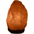 Lampe en sel de l'Himalaya de forme brute posée sur un socle noir, diffusant une lumière orangée.