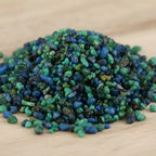 Gros plan sur un monticule de grains d'encens de résine Lavande, montrant un mélange dense de bleu électrique, de turquoise et de vert foncé, sur une surface en bois clair.