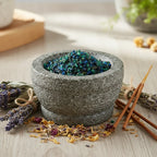 Morceaux de résine Asa Foetida (brun-caramel) dans un mortier en granit gris avec pilon, entouré de sauge, de lavande et de bâtonnets d'encens.