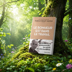 Livre Le Bonheur est dans le Travail - Thich Nhat Hanh sur mousse sacrée au pied d'un arbre, entouré de fleurs violettes sous des rayons de soleil magiques.