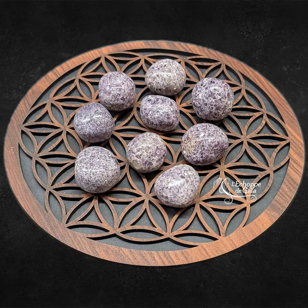 Neuf pierres de lépidolite roulées aux teintes mauves mouchetées et aux surfaces scintillantes, disposées sur un plateau en bois sculpté du motif de la "Fleur de Vie".