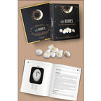 Coffret Les Runes avec livre et runes en agate, boîte noire et or, pierres blanches gravées et pages intérieures du guide ouvertes.