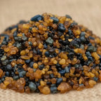 Gros plan sur des grains de résine d’encens de Lourdes ambrés et noirs sur fond naturel.
