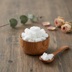 Morceaux de résine ou grains de Manne (couleur blanc pur et opaque), dans un petit bol en bois clair avec une cuillère, sur une planche de bois rustique.