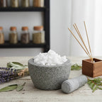 Morceaux de résine ou grains de Manne (blanc pur) dans un mortier en granit gris avec pilon, entouré de sauge, de lavande et de bâtonnets d'encens.