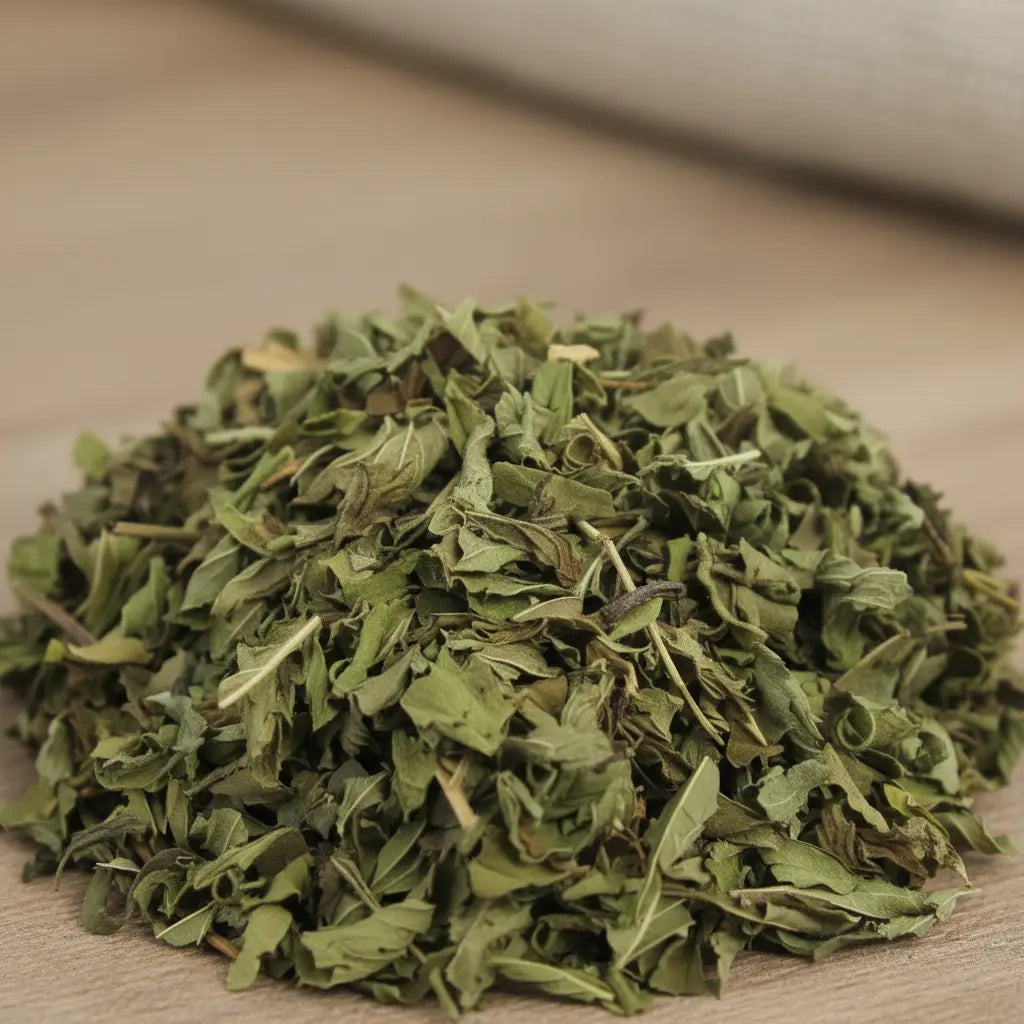 Gros plan sur des feuilles de menthe séchées, en copeaux verts formant un petit tas sur une table en bois.