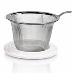 Filtre infuseur de thé amovible en acier inoxydable tressé muni d'une poignée, posé sur un couvercle rond en porcelaine blanche.