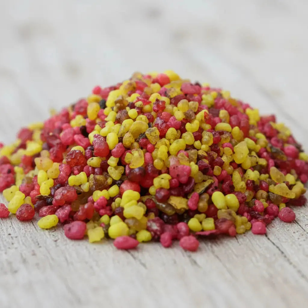 Gros plan sur un monticule de grains d'encens de résine Nazareth, montrant un mélange vif de couleurs rouge, rose fuchsia et jaune doré, sur une surface en bois clair.